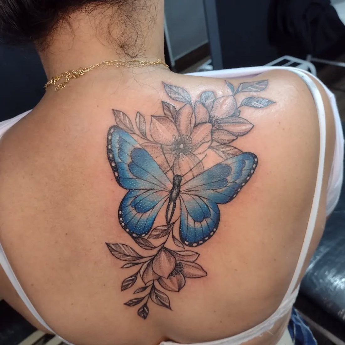 Tatuagem colorida de borboleta azul com flores nas costas