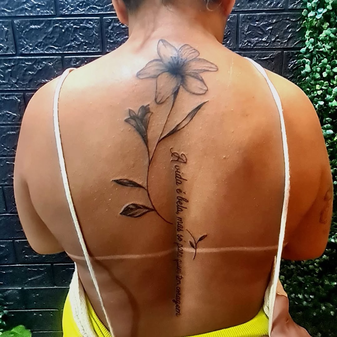 Tatuagem fine line de lírio com frase ao longo da coluna